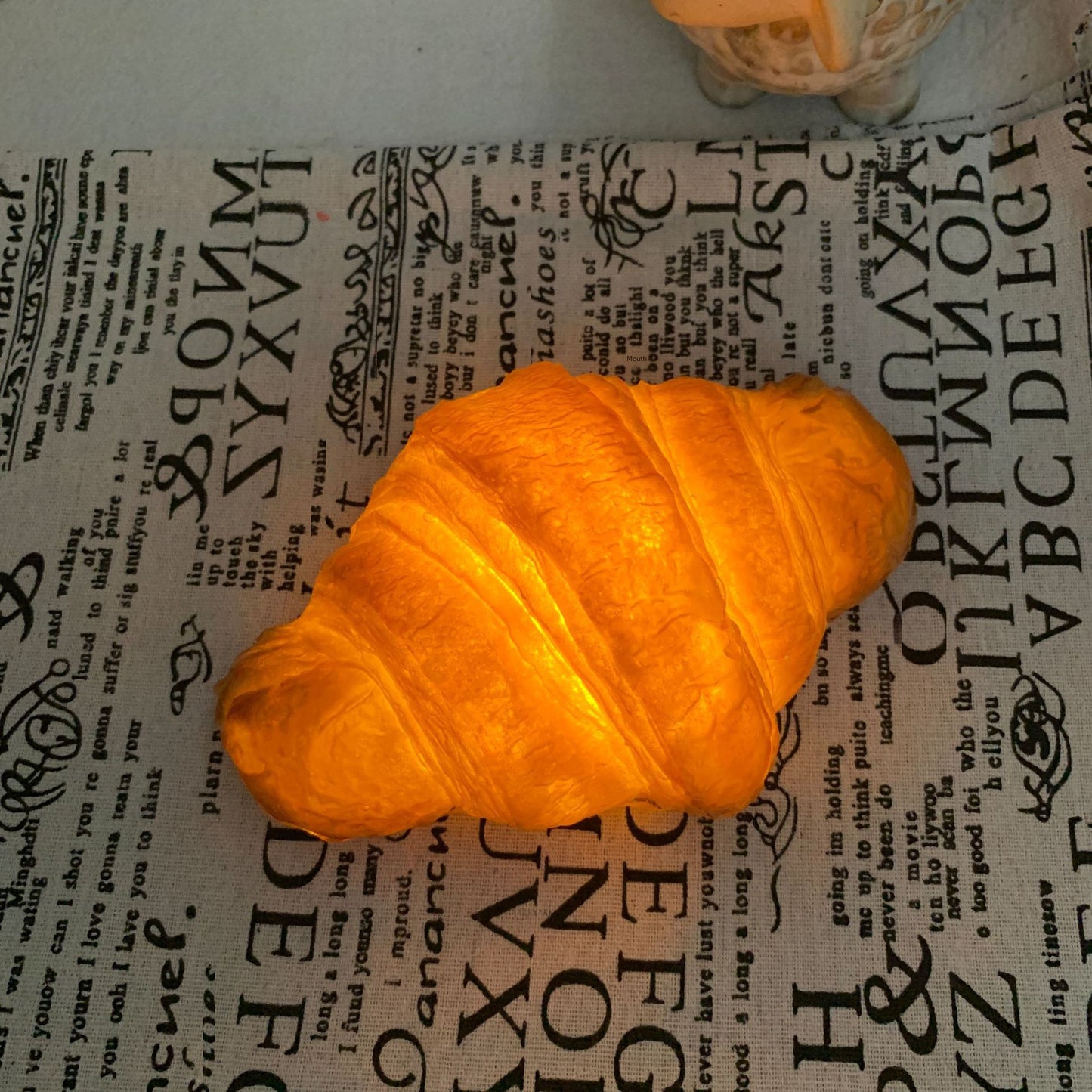 CroissantGlow™ LED bread night light in warm white on a bedside table
