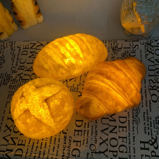 CroissantGlow™ LED bread night light in warm white on a bedside table
