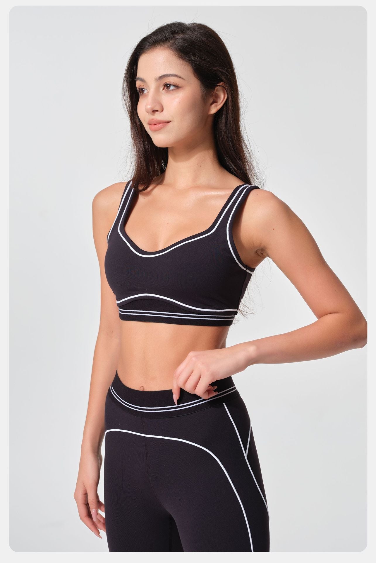 Woman wearing a black sports bra and leggings with white accents on a light gray background