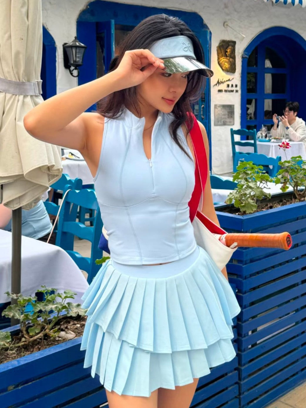 Woman in light blue tennis outfit with visor and racket in a Mediterranean-style setting
