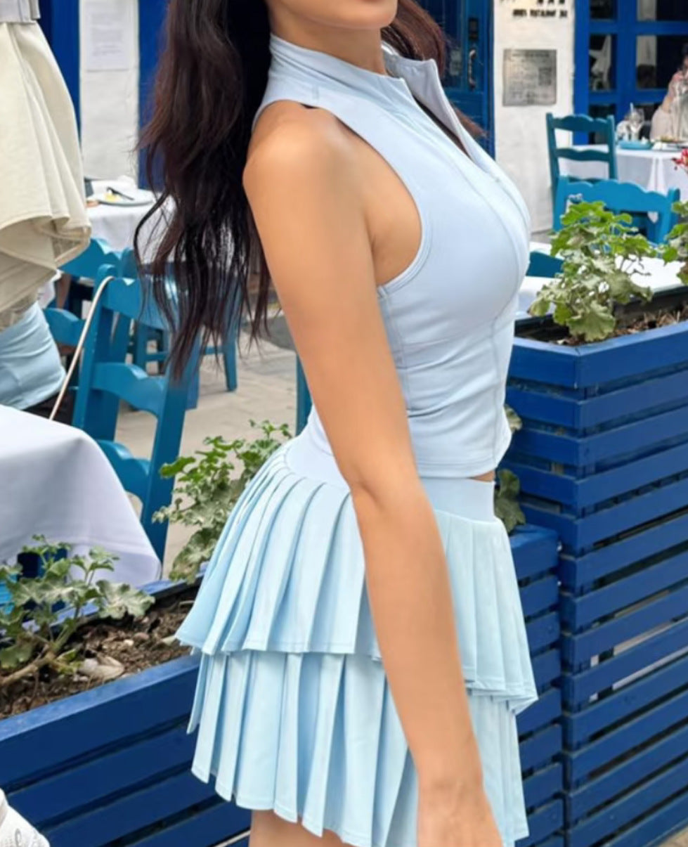 Woman in a light blue dress standing in an outdoor setting with blue chairs and tables.