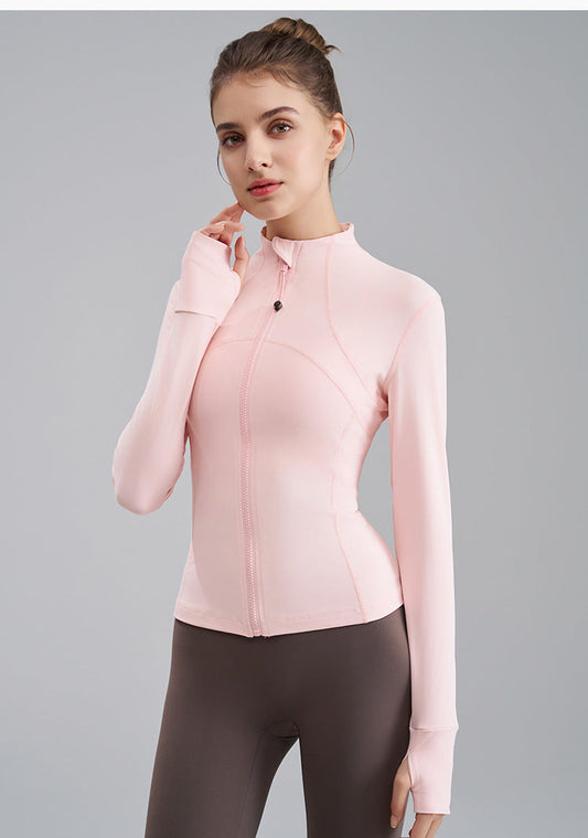 Woman wearing a light pink jacket and dark gray leggings on a gray background