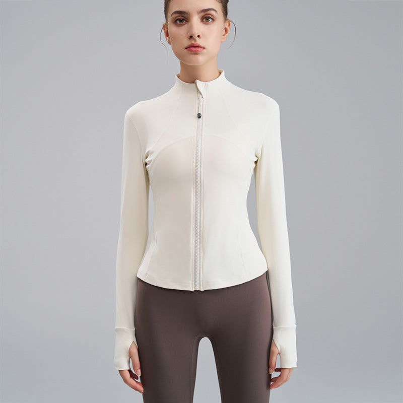 Woman wearing a white zip-up athletic jacket and brown leggings on a gray background